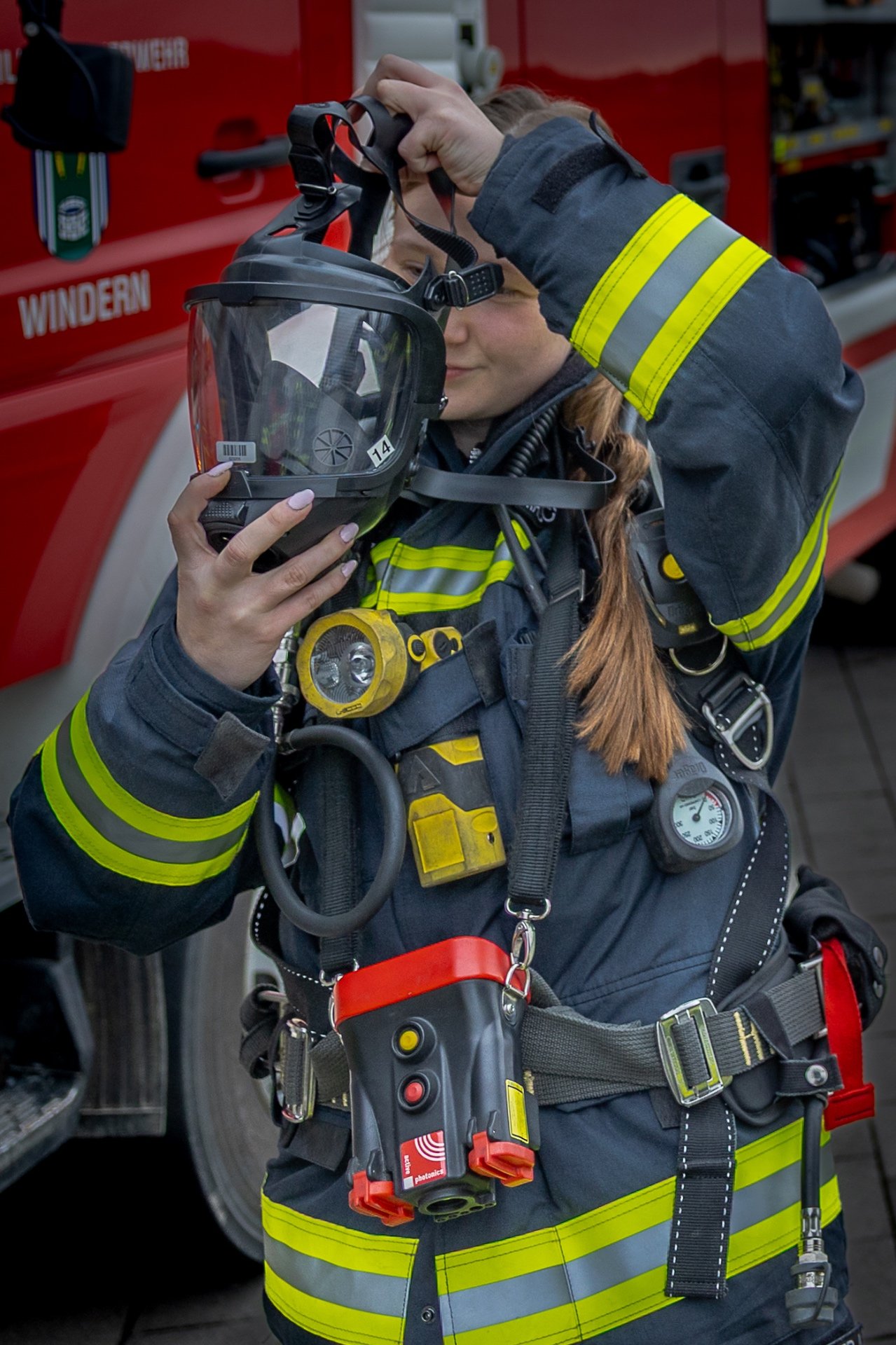 Feuerwehrfrau legt vor einem Feuerwehrfahrzeug ihre Atemschutzmaske an